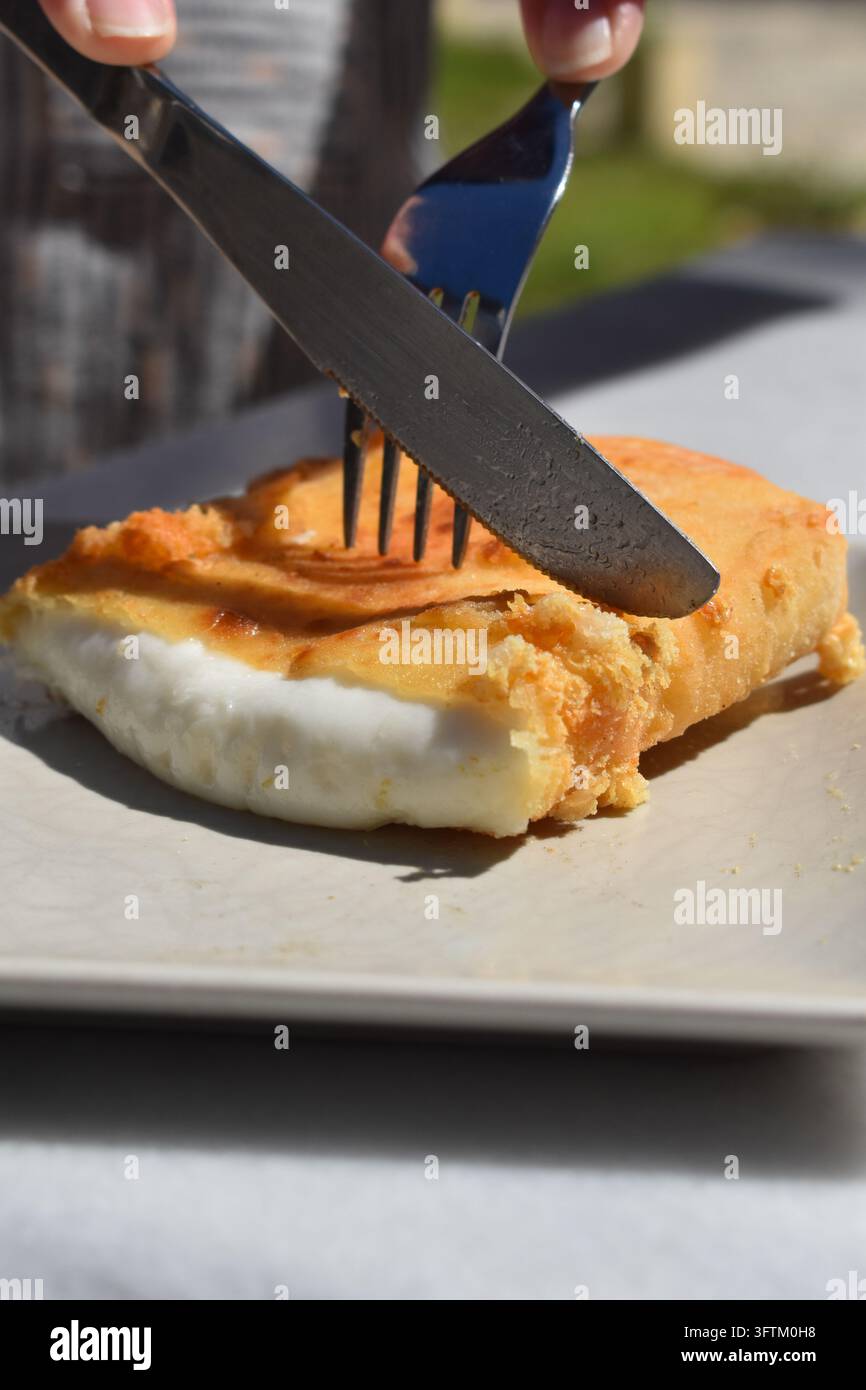 Antipasto greco tradizionale di formaggio fritto saganaki tagliato con coltello e forchetta in un ristorante all'aperto Foto Stock