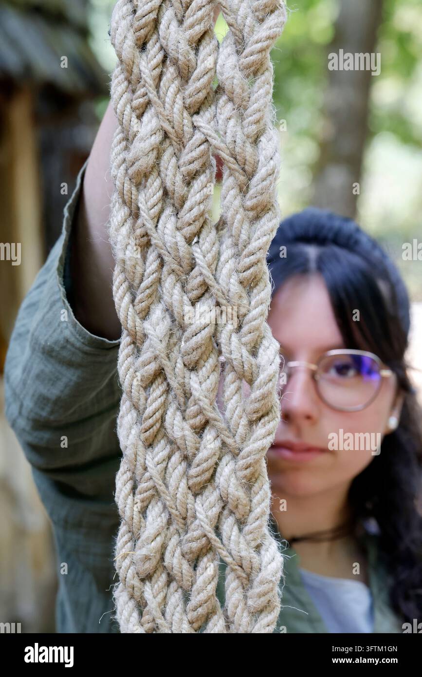 Una giovane donna tiene una corda intrecciata artigianale fatta di fibre naturali nel cantiere medievale del castello di Guédelon. Treigny, Francia. Foto Stock