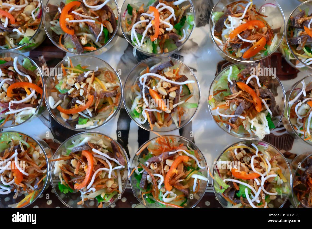 Diversi bicchierini pieni di insalata asiatica e guarniti con verdure croccanti, pezzi di carne, vermicelli e arachidi sono disposti in fila per un a Foto Stock