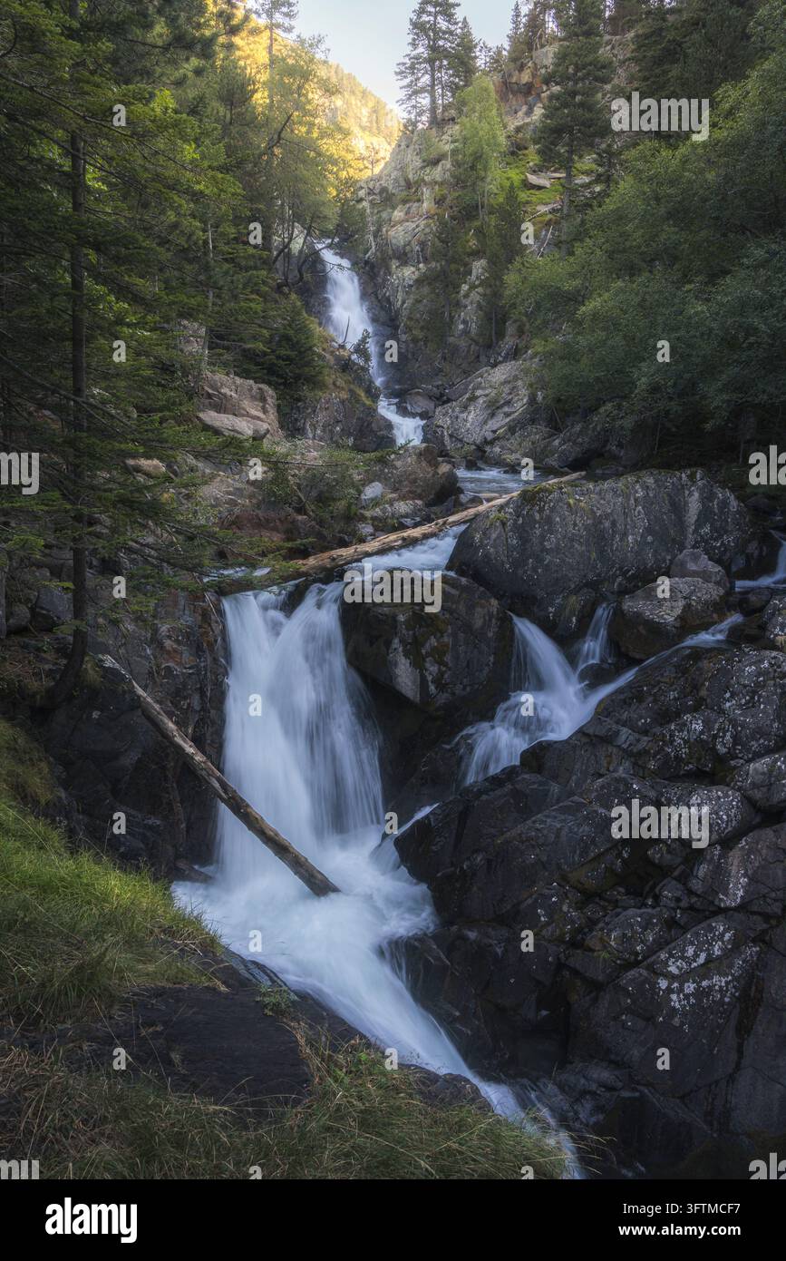 L'acqua cade sulle rocce scure sotto le scogliere boscose a Gorgas de Alba nella valle di Benasque, Pirenei spagnoli, nella luce soffusa. Foto Stock
