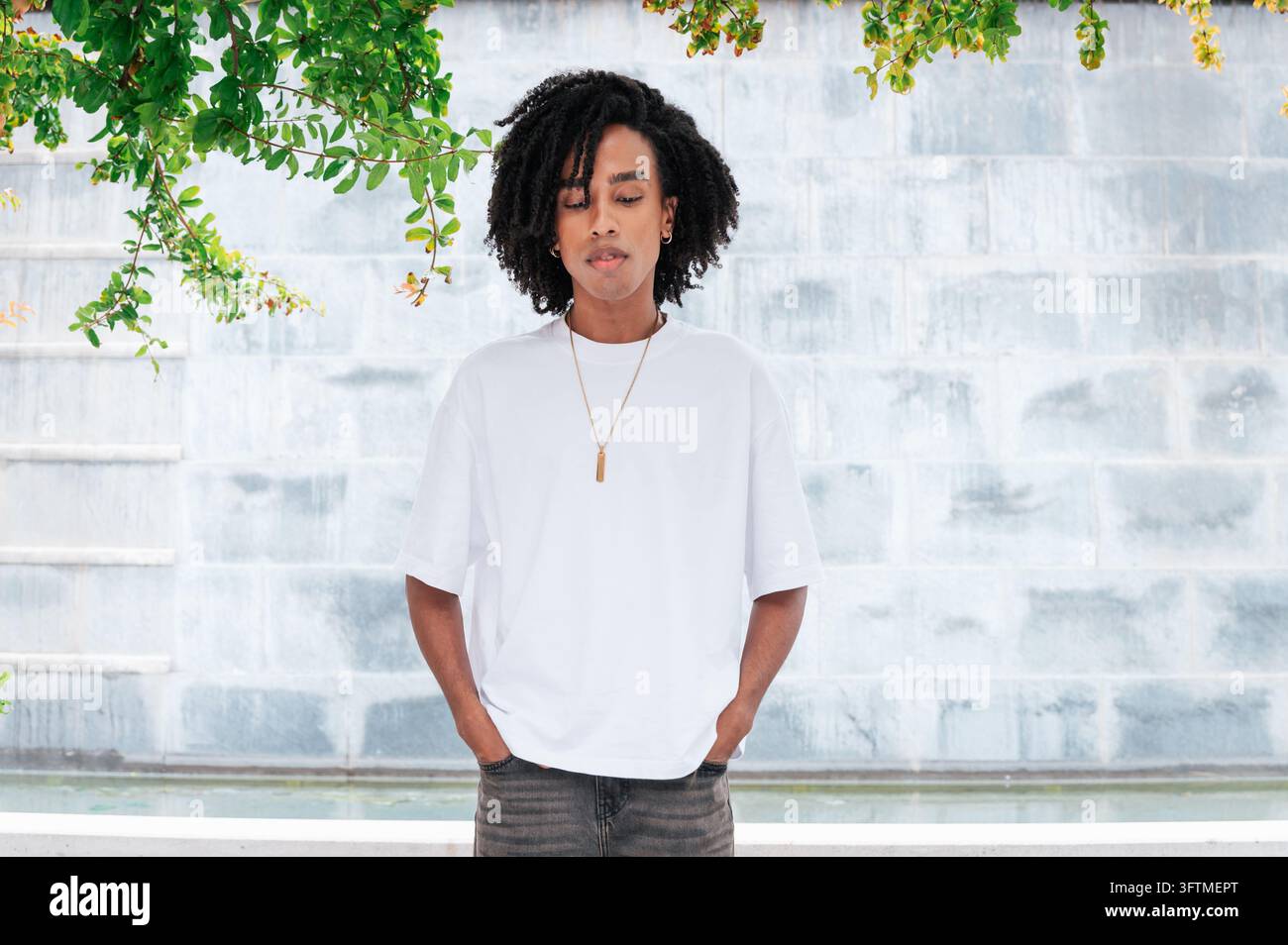 Giovane uomo con dreadlocks che indossa una maglietta oversize, in piedi all'aperto Foto Stock