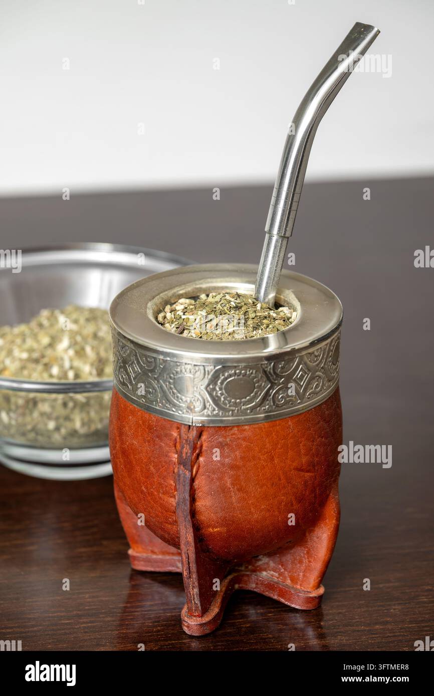 Calebasse tradizionale argentina per il mate con yerba mate e bombilla in metallo su un tavolo di legno, preparazione di una bevanda alle erbe Foto Stock