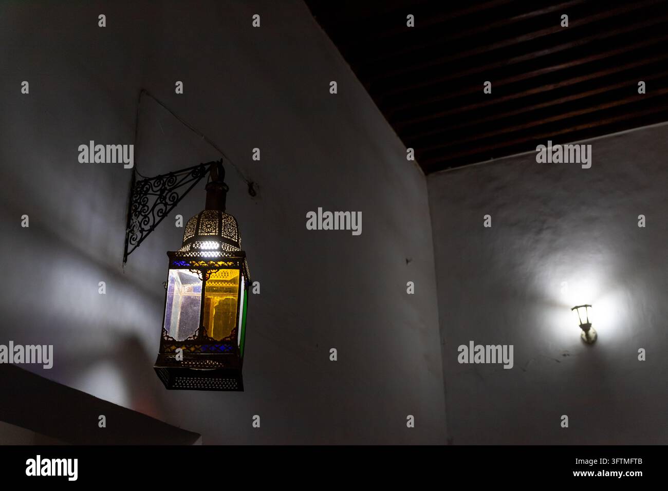 Primo piano di una lanterna sospesa in ferro ornata con vetri colorati gialli, viola e verdi montata su un muro bianco a Marrakesh, Marocco.... Foto Stock