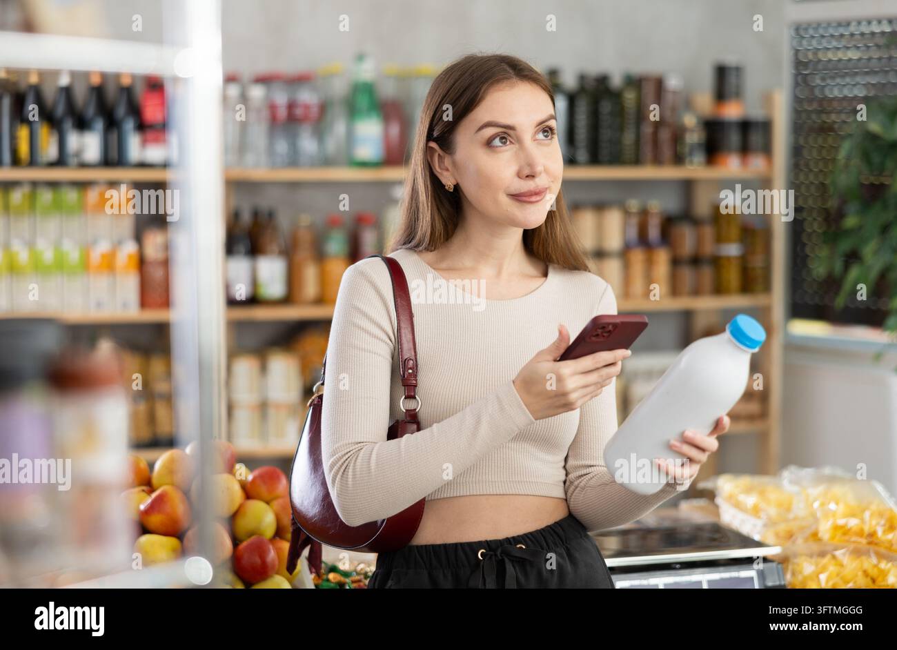 L'acquirente donna verifica l'idoneità - scansiona il codice QR sull'etichetta del flacone di latte nel negozio di alimentari Foto Stock