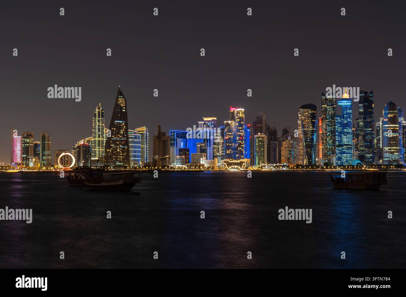 Doha, Qatar - 22 gennaio 2026: Vista notturna a lunga esposizione con teleobiettivo medio della skyline di Doha dalla corniche, evidenziando le tradizionali barche dhow. Foto Stock