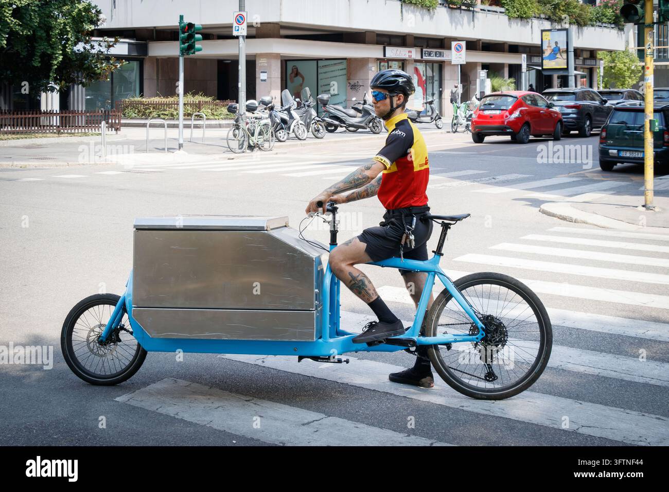 Corriere in bicicletta con carico blu sul passaggio pedonale di una strada cittadina a Milano, Italia Foto Stock