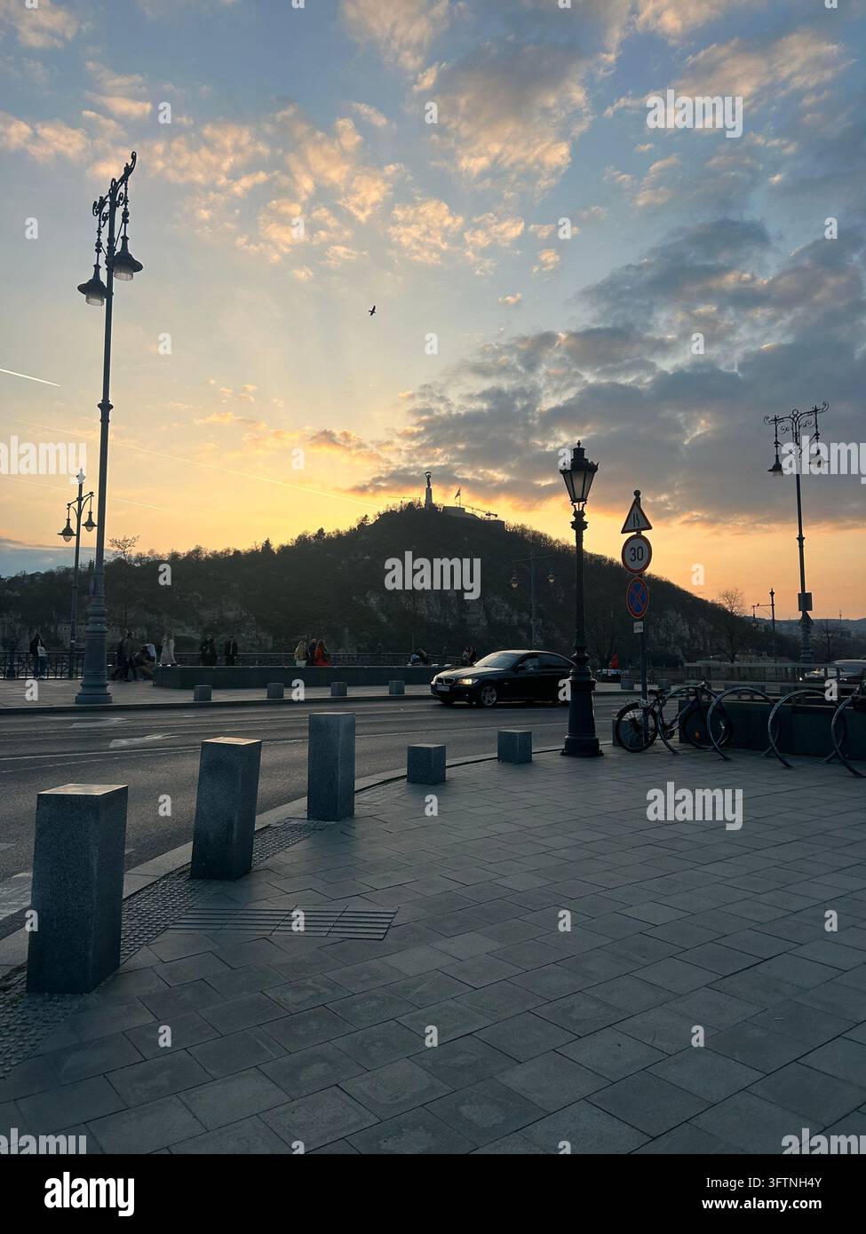 Veduta stradale di Budapest al tramonto con la collina di Gellert, lampioni e traffico serale, Ungheria - Immagine stock catturata con smartphone