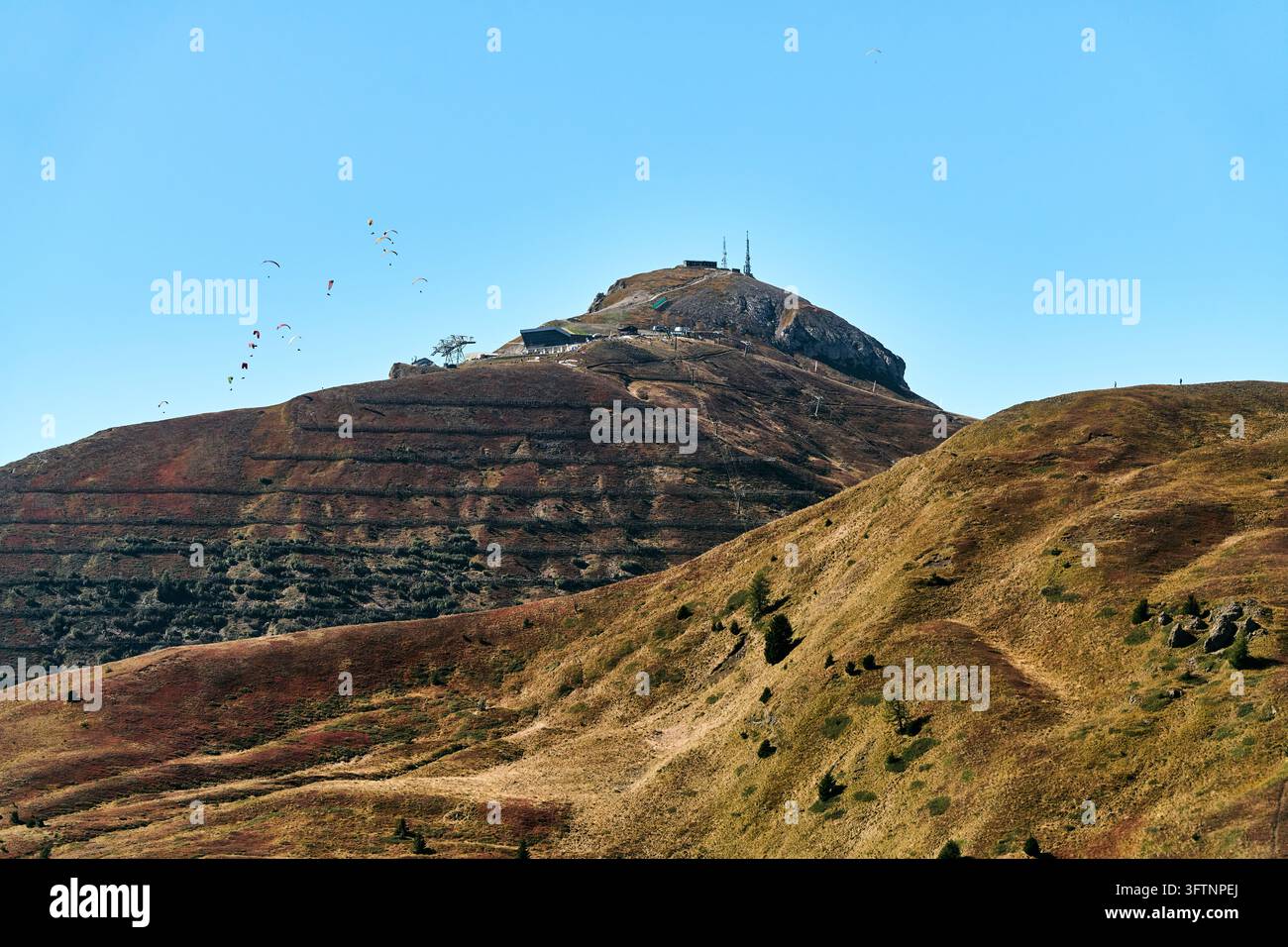 Somma di una collina rocciosa con antenne sopra pendii erbosi ondulati sotto un cielo blu limpido, piccolo stormo di alianti o uccelli visibile in lontananza, autunno caldo Foto Stock