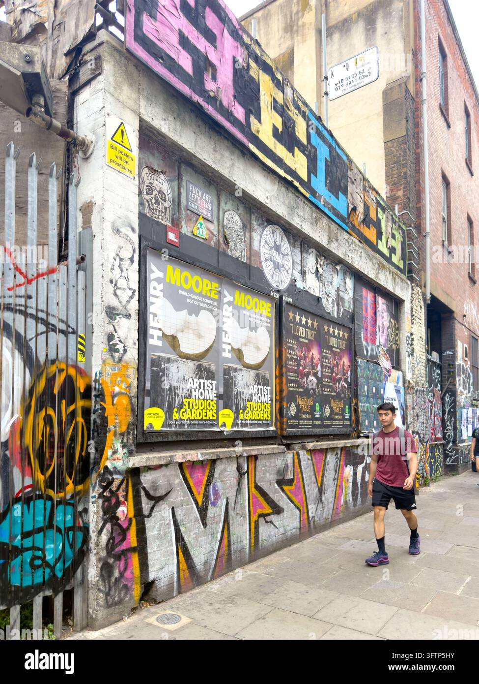 Persona che passa davanti a un edificio con graffiti e poster di Henry Moore a Brick Lane, Londra - Immagine stock catturata con smartphone