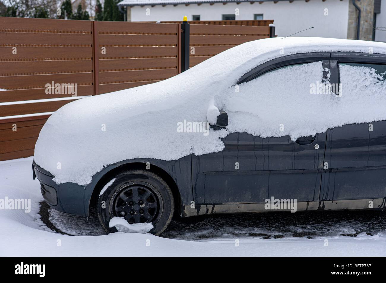 Automobile grigio scuro parcheggiata all'aperto e coperta da uno spesso strato di neve fresca dopo forti nevicate invernali, con finestrini ghiacciati e accumuli di neve Foto Stock
