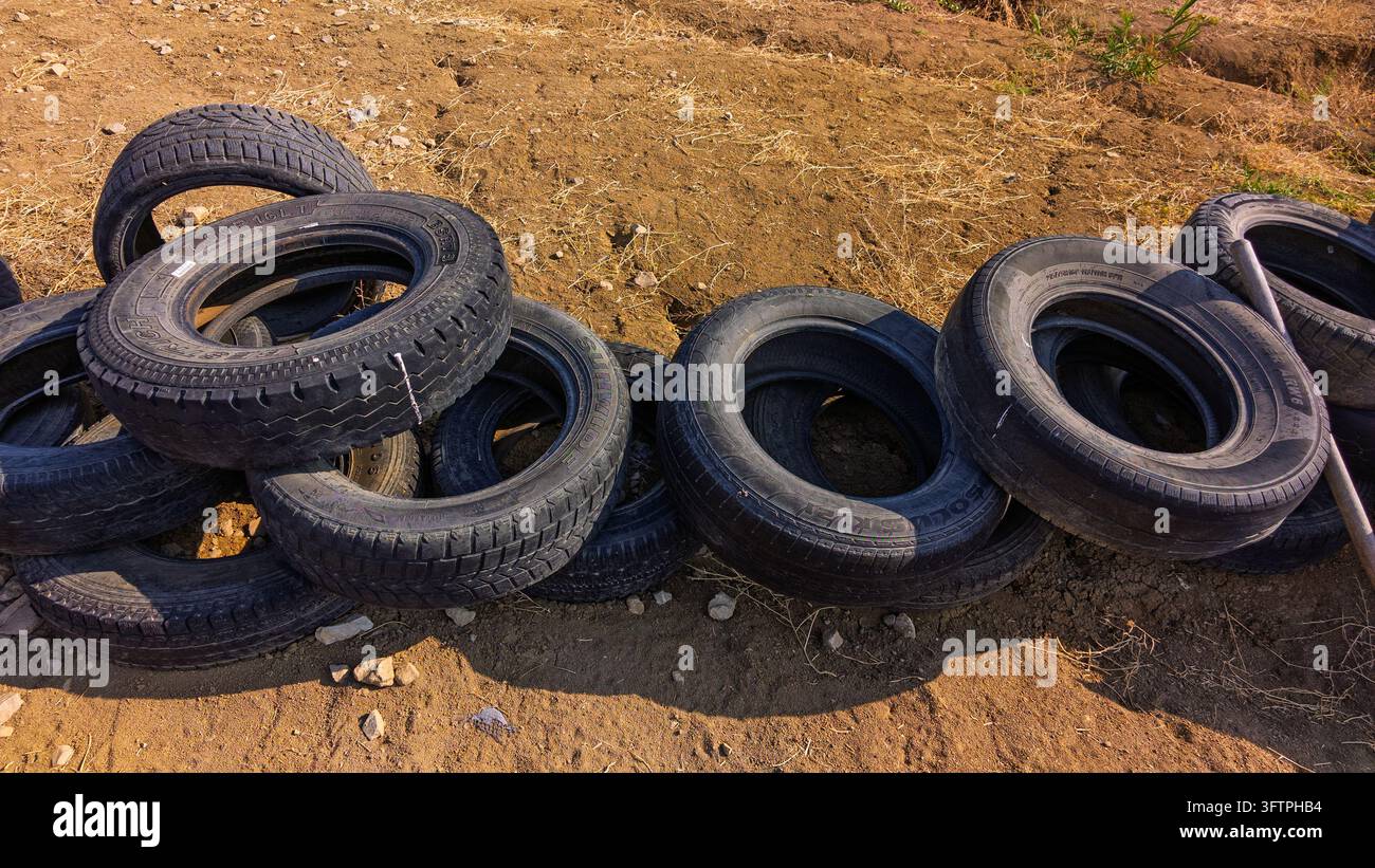 Gomme sparse su un terreno secco e polveroso. La luce del sole evidenzia le superfici di gomma consumate Foto Stock