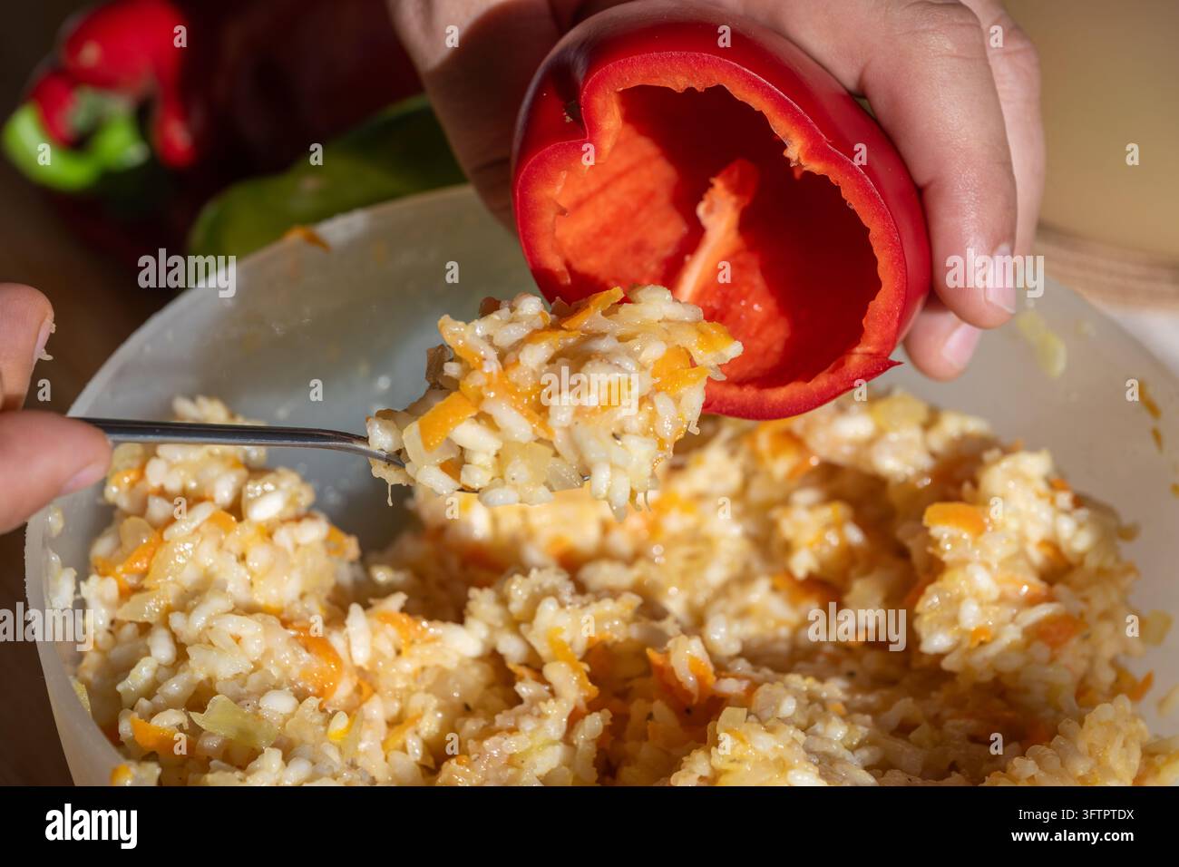 Una persona riempie un peperone rosso svuotato con un miscuglio condito di riso, carne tritata e verdure utilizzando un cucchiaio di metallo alla luce naturale. Foto Stock