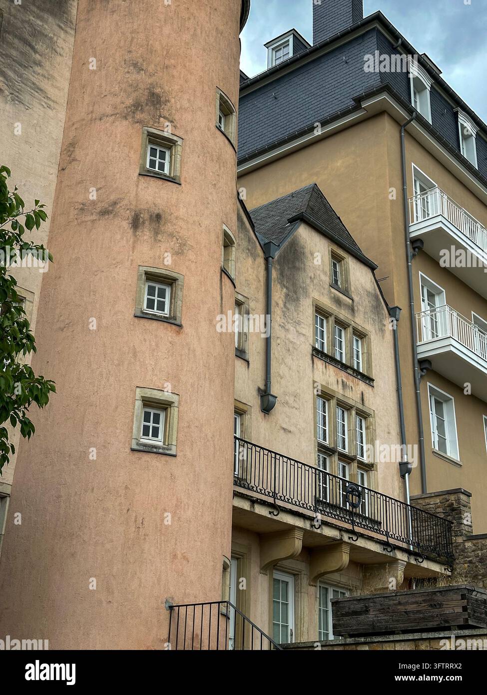 Facciata di edificio europeo antico con torre rotonda e balcone. Una torre rotonda di pesche si trova accanto a un edificio europeo classico con una ferriera nera - Immagine stock catturata con smartphone