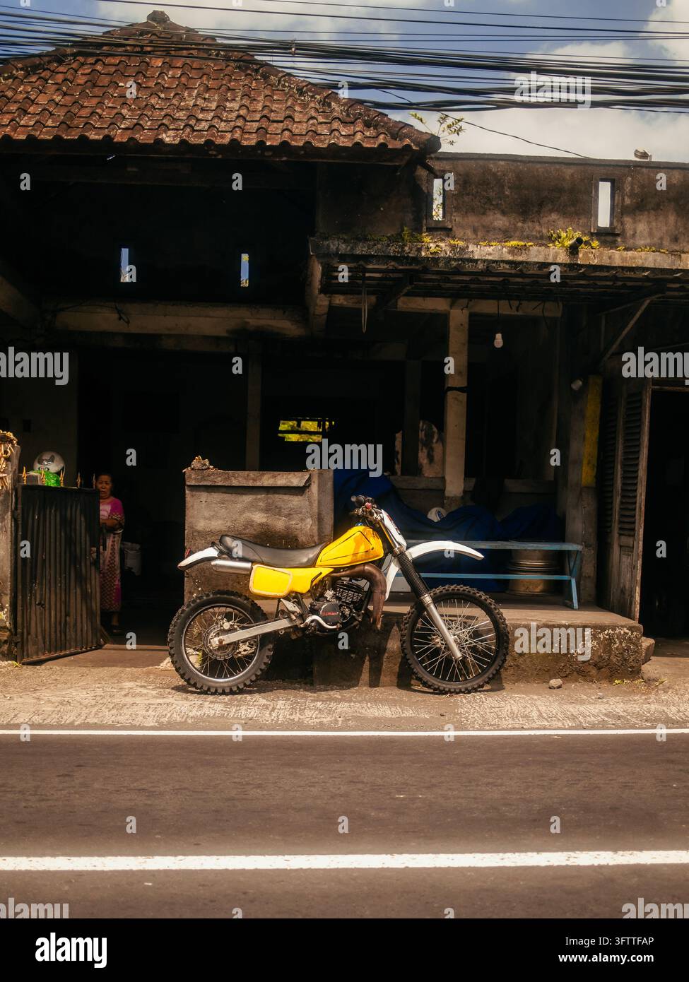 Sidemen, Bali, Indonesia - 08 agosto 2026: Vista di una moto gialla parcheggiata davanti a un edificio tradizionale con tetto a tegole. Foto Stock
