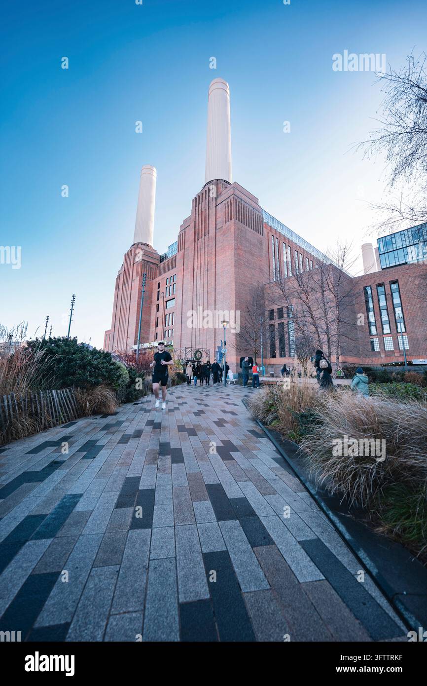 Persone che camminano lungo un sentiero lastricato verso l'imponente centrale elettrica in mattoni con le sue alte ciminiere, Londra, Regno Unito Foto Stock