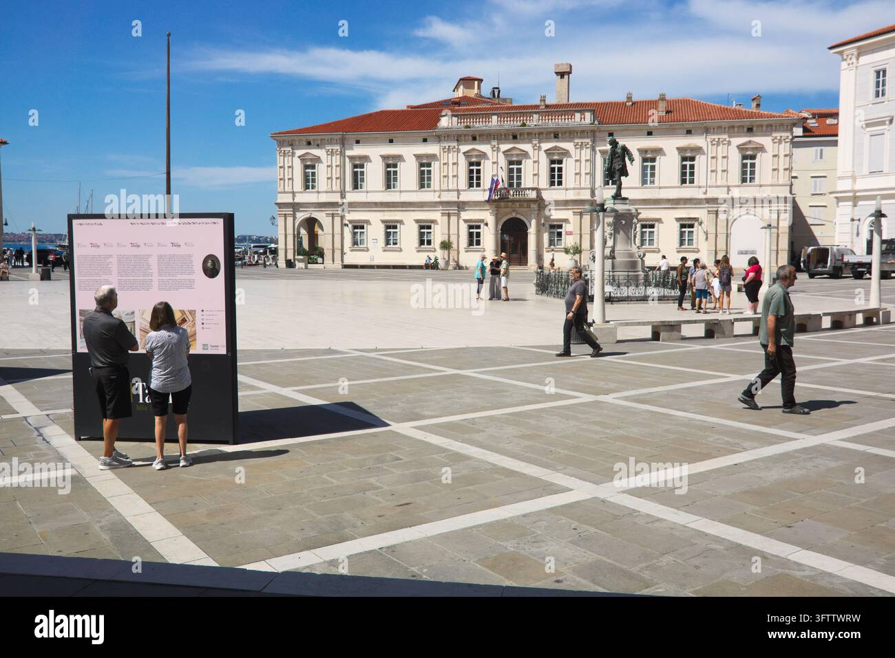 Visitatori su Piazza Tartini che guardano una tavola informativa vicino alla statua di Tartini e al Palazzo della Corte a Piran, in Slovenia. Foto Stock
