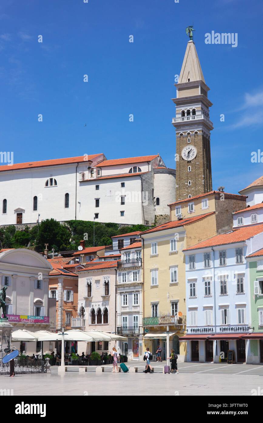 Piazza Tartini e edifici veneziani colorati sotto la chiesa parrocchiale di San Giorgio e il campanile sotto un cielo blu a Pirano, in Slovenia. Foto Stock