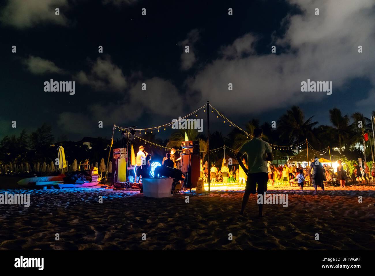 Grand World, Phu Quoc, Vietnam - 12 aprile 2026: I visitatori si radunano vicino a un palco sulla spiaggia durante un evento di intrattenimento serale con musica dal vivo, luci Foto Stock
