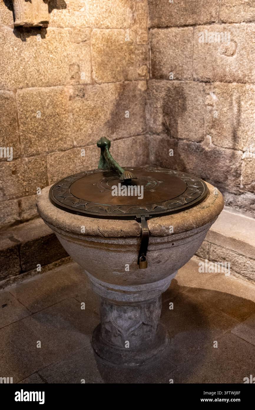 Antica fontana battesimale in pietra con coperchio in bronzo decorato e maniglia simbolica all'interno della Cattedrale di Santiago di Compostela, Spagna – 20 luglio 2026 Foto Stock