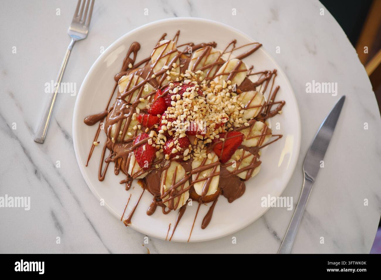 Waffle servito su un piatto bianco, guarnito con fette di banane, fragole, salsa al cioccolato. Foto Stock