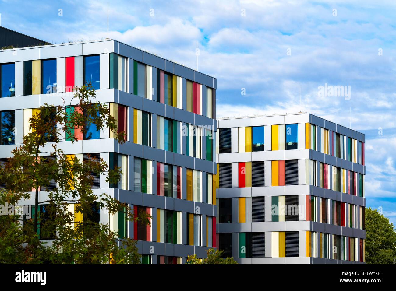 Edificio moderno d'ufficio con sezioni di facciata contrastanti bianche e scure, finestre rettangolari ripetute e accenti arancioni. La luce del sole evidenzia le Foto Stock
