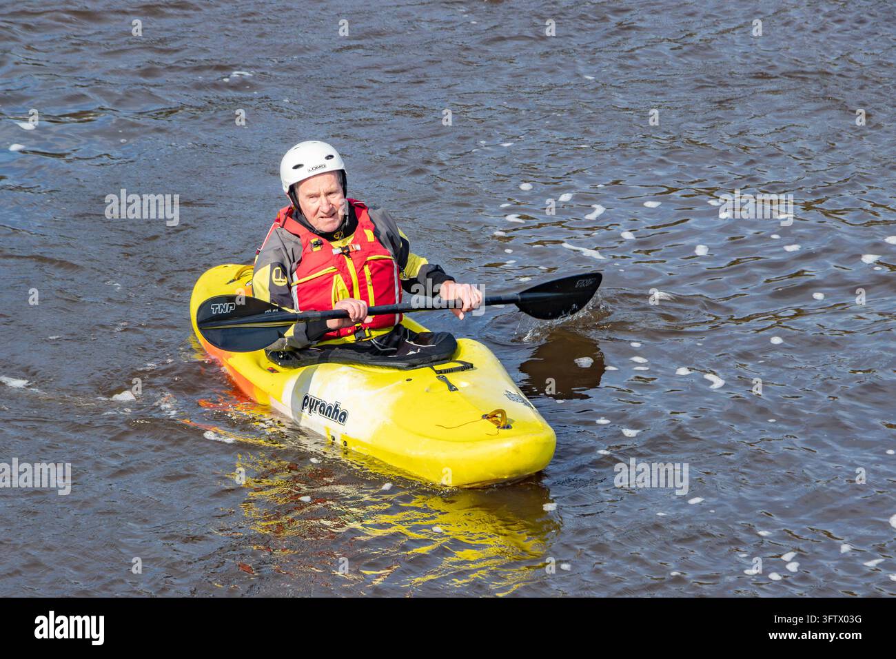 Kayaker che rema in un kayak Pyranha con una pagaia TNP sull'acqua del fiume, indossando casco e giubbotto di salvataggio Foto Stock
