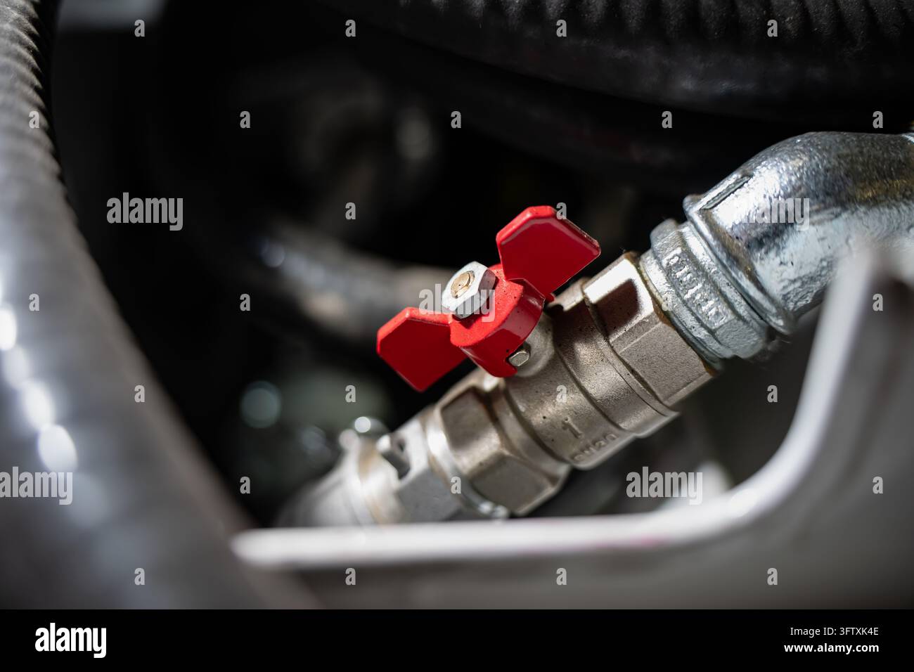 Valvola a sfera con maniglia a farfalla e connessioni filettate in metallo all'interno di un assemblaggio di apparecchiature, che mostra hardware di isolamento del flusso manuale per l'impianto idraulico Foto Stock