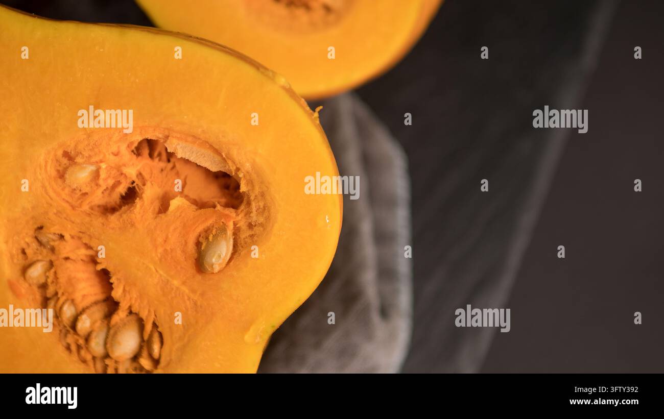 Zucca arancione tagliata a metà con semi visibili e centro fibroso disposta su una superficie scura e strutturata in primo piano vista dall'alto di prodotti freschi Foto Stock