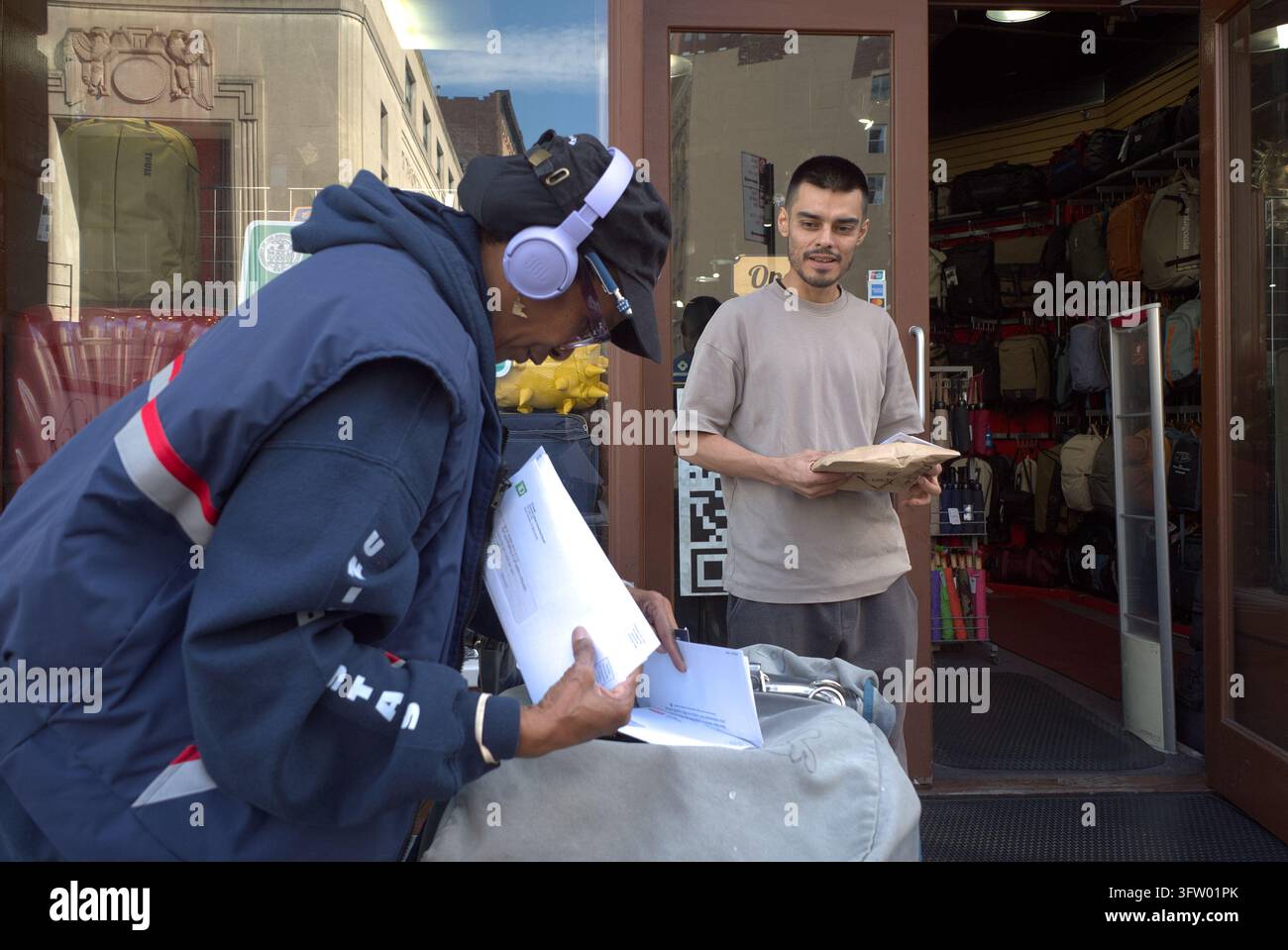 Un addetto alla consegna della United States Postal Service (USPS) smista le lettere mentre un uomo aspetta la sua consegna a Manhattan, illustrando la distribuzione quotidiana della posta Foto Stock