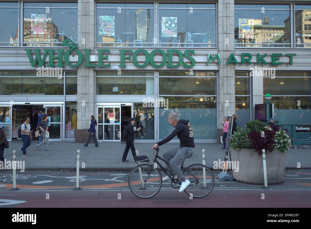 New York, USA. Un uomo in bicicletta davanti a un negozio Whole Foods Market vicino a Union Square a Manhattan, evidenziando la vita quotidiana di strada e urbana Foto Stock