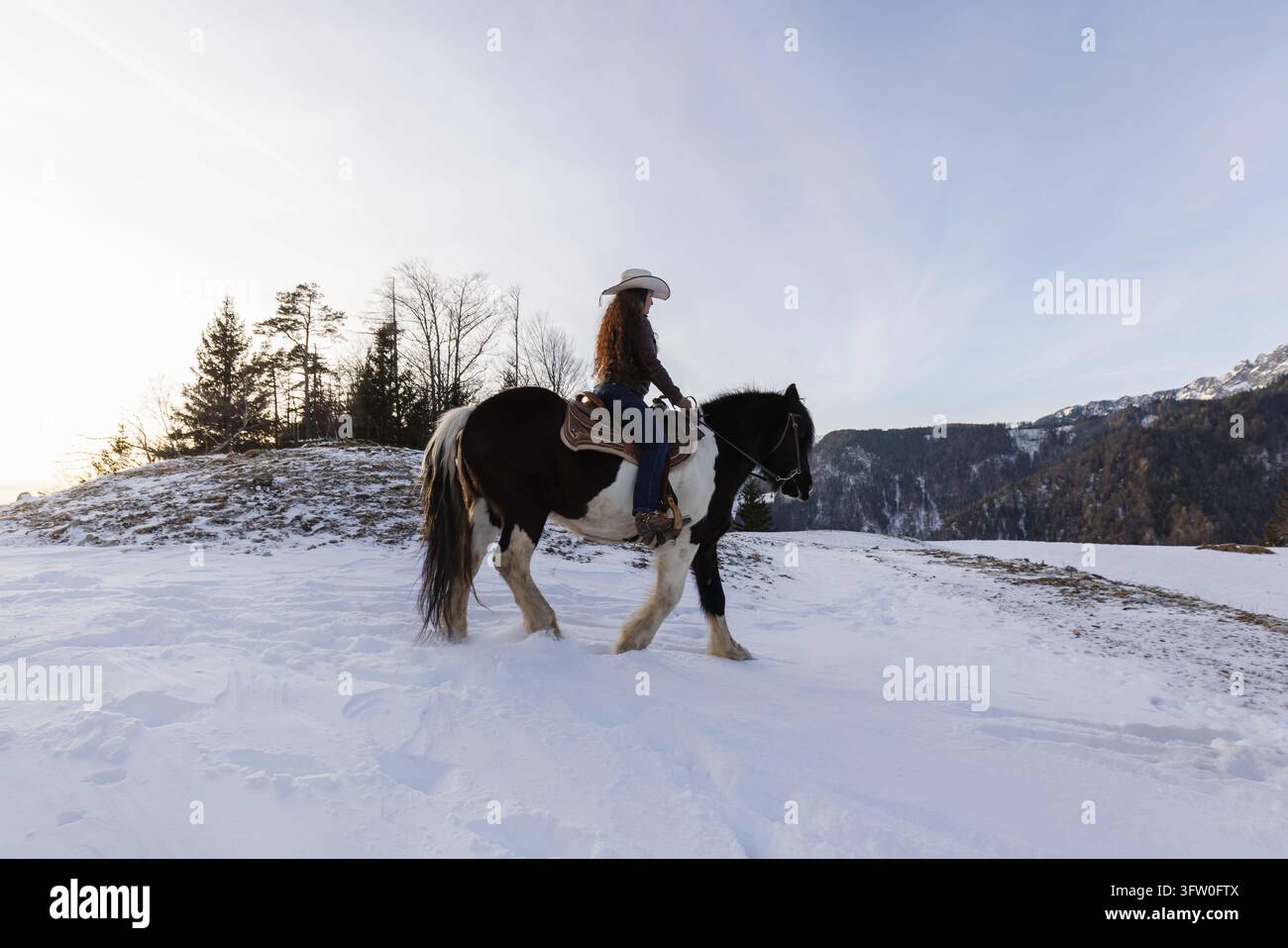 Cavallerizza che si rilassa a cavallo nella pacifica natura invernale, connettendosi con il suo cavallo mentre gode dello stile di vita equestre. Foto Stock