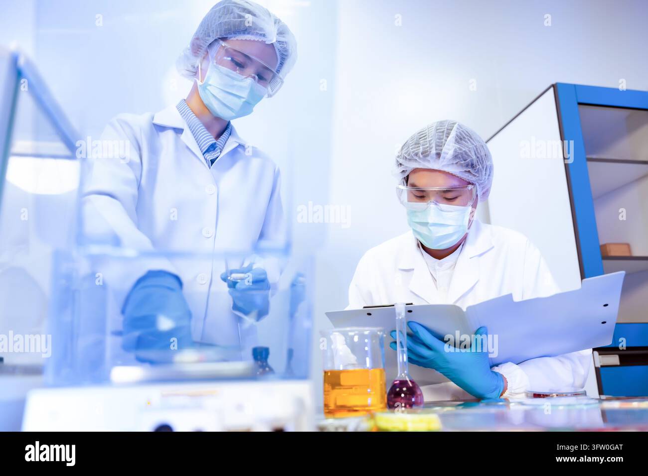 Squadra di scienziati asiatici che misura un campione di capsula di pillola su una bilancia digitale, concetto di controllo qualità in laboratorio di ricerca farmaceutica Foto Stock
