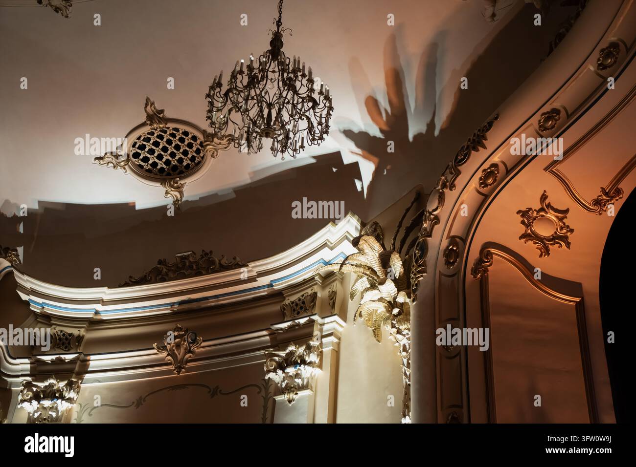 Un lampadario ornato pende accanto a una griglia a soffitto ovale e a elaborate modanature in stucco, illustrando elementi decorativi del soffitto e ornamenti architettonici Foto Stock