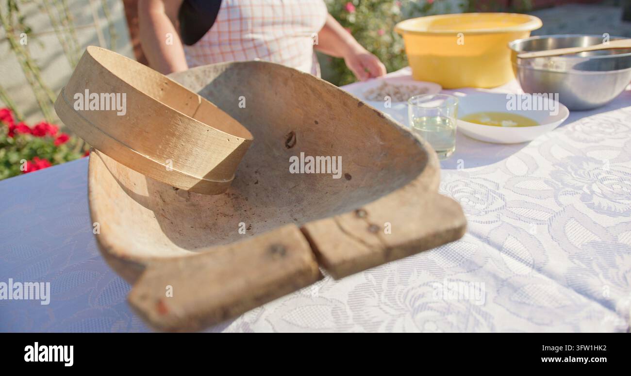 Vecchio troppone di pasta di legno con setaccio rotondo di legno su tovaglia bianca a fantasia all'aperto sotto illuminazione calda di luce del giorno che riempie il primo piano con la cottura Foto Stock