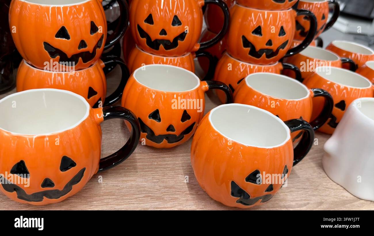 Tazze di ceramica a forma di zucche di Halloween arancioni con manici neri esposti su uno scaffale del negozio per Halloween. Foto Stock