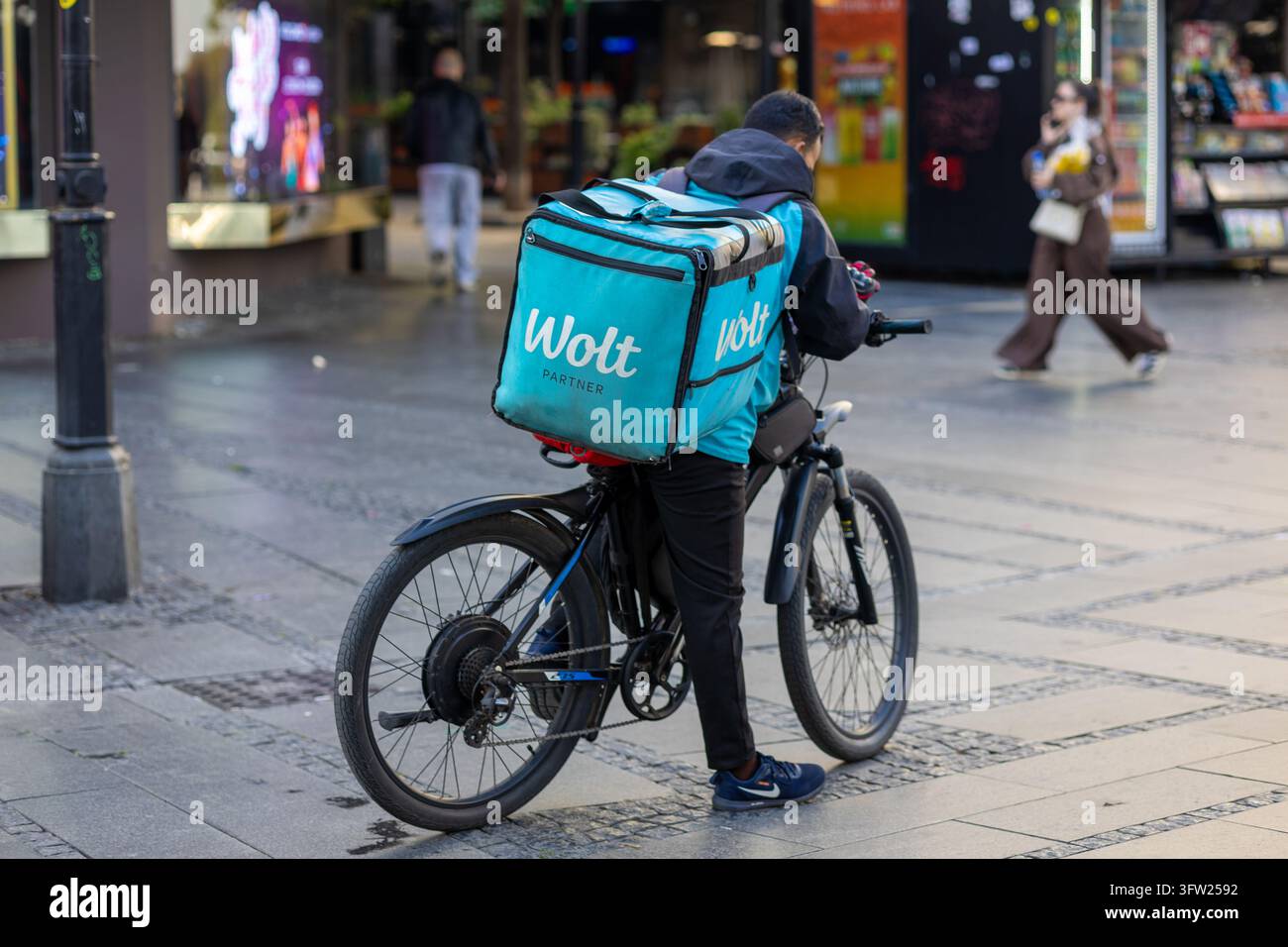 BELGRADO, SERBIA - 29 SETTEMBRE 2026: Un corriere di consegna Wolt con una grande borsa di consegna con marchio è seduto su una bicicletta elettrica e controlla il navigazione Foto Stock