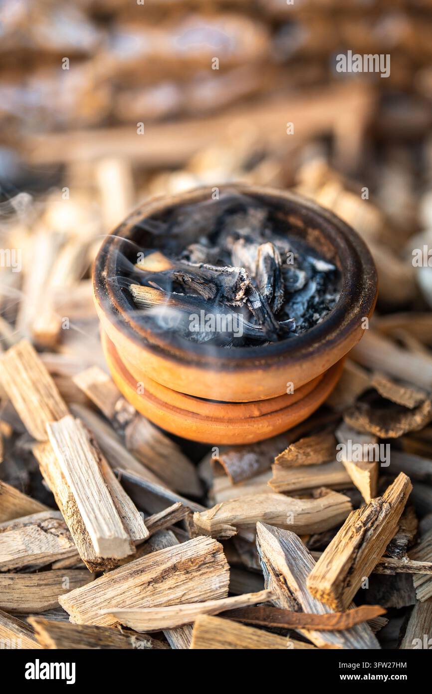 Pentola di argilla con bastoncini fumanti circondata da materiali tradizionali per la preparazione di incenso alle erbe Foto Stock