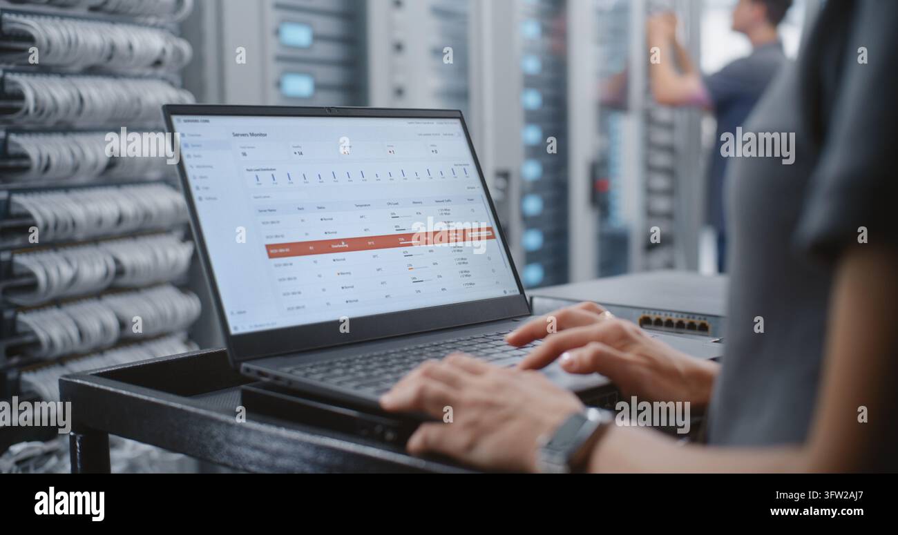 Specialista femminile del data center monitora il dashboard del server mentre appare un avviso critico di surriscaldamento, rivedendo la temperatura, il carico della CPU, la memoria e il traffico di rete mentre avvia le procedure di risposta agli incidenti. Foto Stock