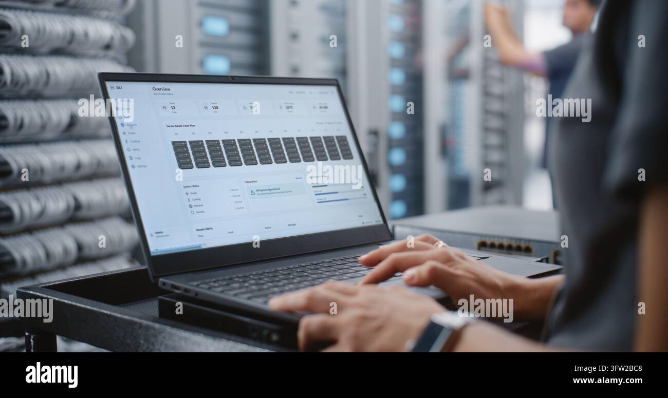 Ingegnera di Data Center monitora la telemetria dei server su laptop, indagando su un allarme critico di surriscaldamento mentre controlla le temperature dei rack, l'alimentazione, il raffreddamento e le prestazioni di rete in tempo reale. Foto Stock