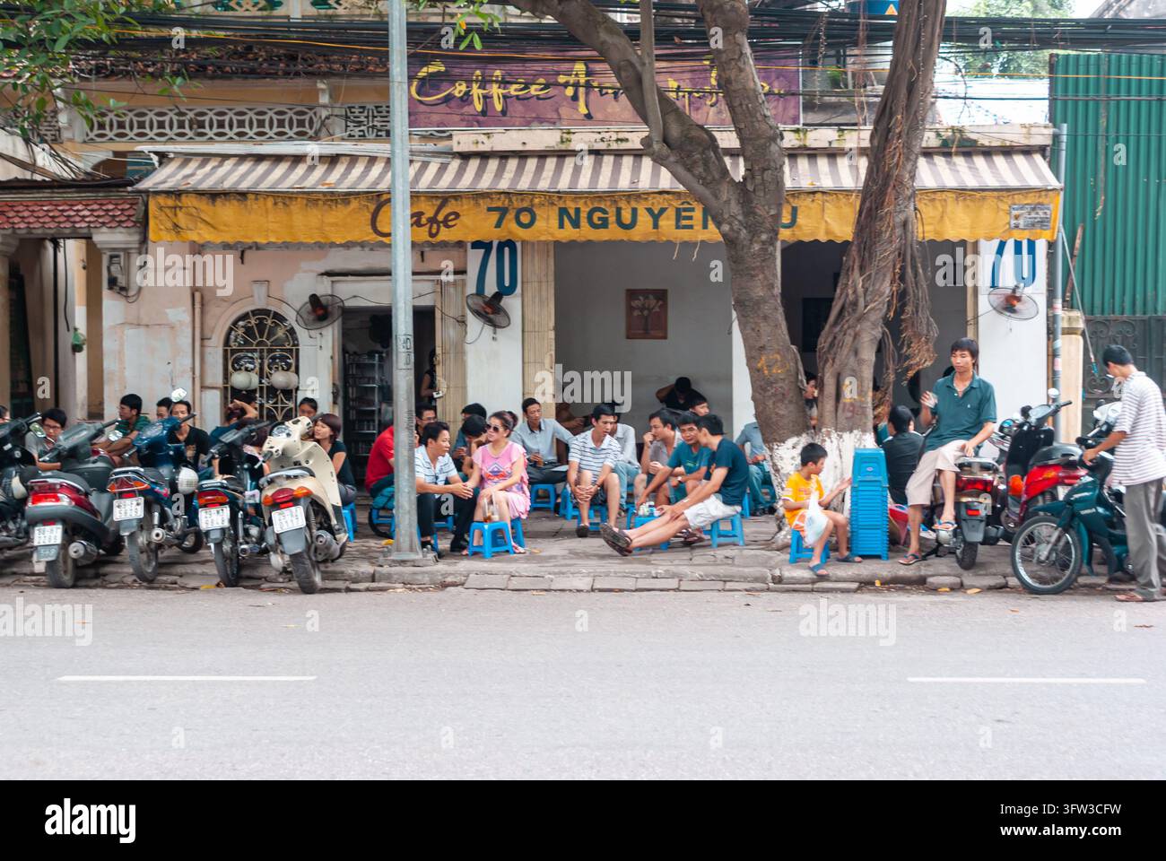 HANOI, VIETNAM - 16 LUGLIO 2011: Persone sedute su piccoli sgabelli di plastica fuori da un caffè sul marciapiede in Nguyen Du Street a Hanoi, Vietnam, mentre le moto Foto Stock