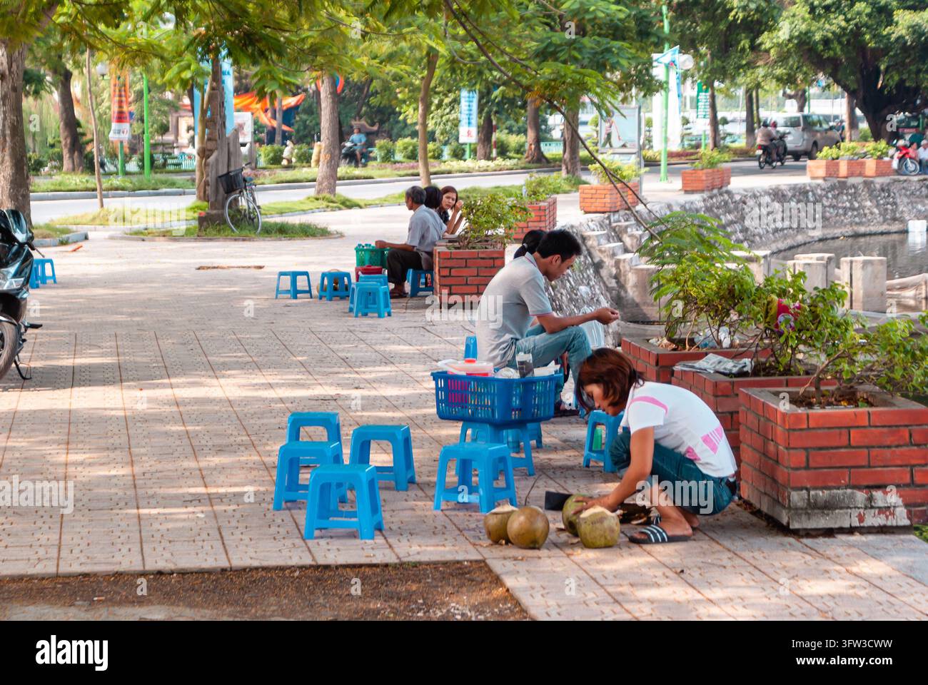 HANOI, VIETNAM - 17 LUGLIO 2011: I residenti locali siedono su piccoli sgabelli di plastica lungo la passeggiata sul lungolago del West Lake a Hanoi, Vietnam, mentre un str Foto Stock