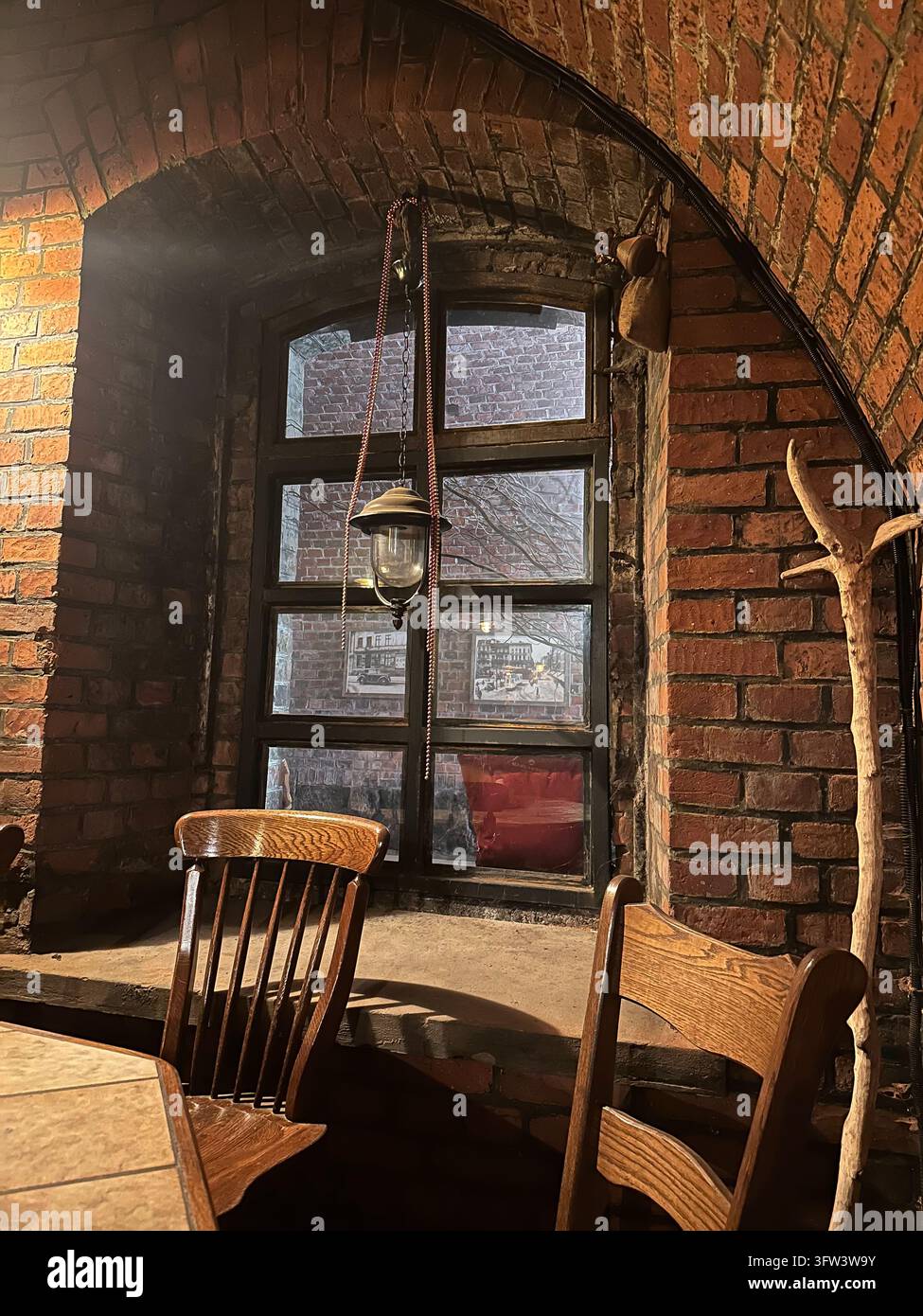 Interno accogliente di un caffè con arco in mattoni rossi, sedie di legno e lampada sospesa. - Immagine stock catturata con smartphone