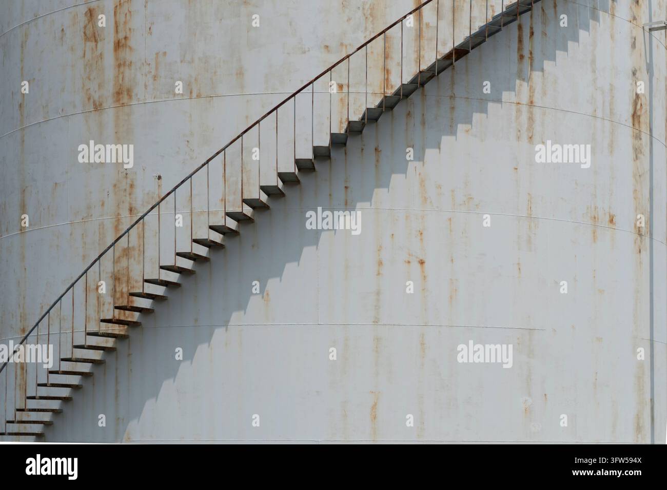 Scala a chiocciola sul lato di un vecchio serbatoio di olio bianco arrugginito Foto Stock