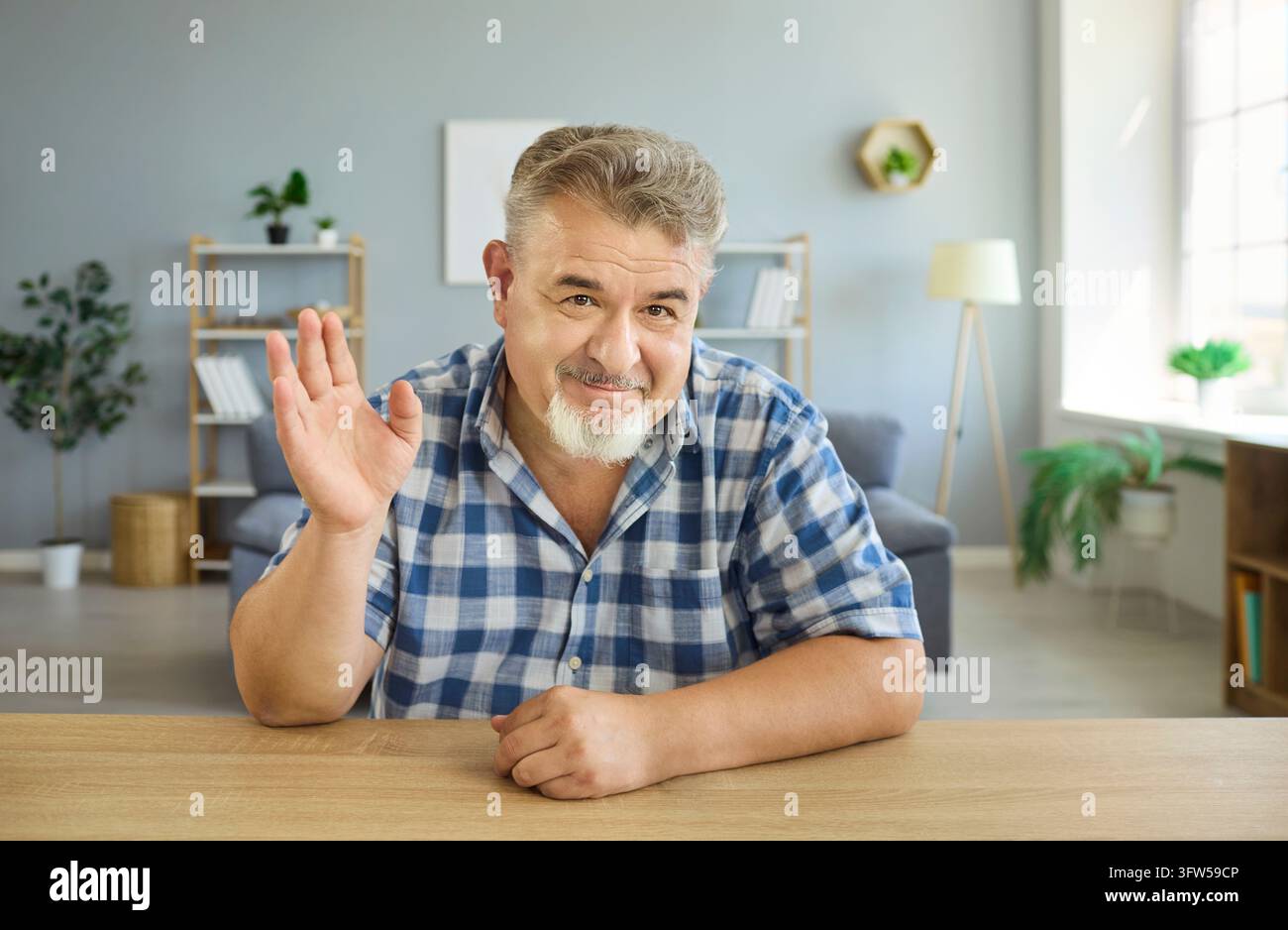 Anziano allegro che saluta la telecamera durante una videochiamata online da casa Foto Stock