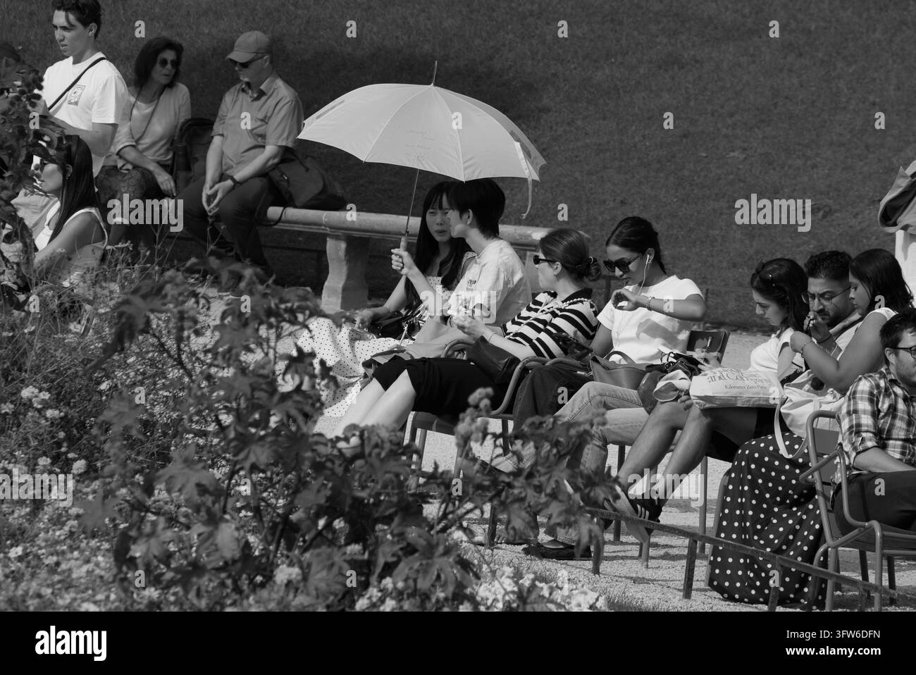 Fotografia di strada in bianco e nero di turisti e locali seduti su sedie da parco verdi che si rilassano sotto un ombrellone nel Jardin des Tuileries, Parigi, Francia Foto Stock