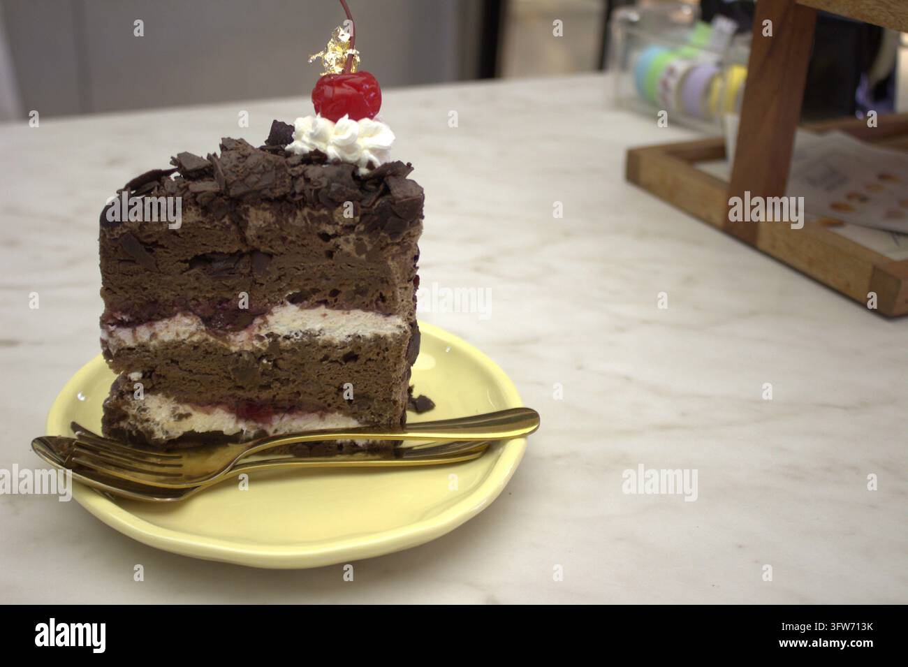 Torta della Foresta Nera ricoperta di ciliegie e foglia d'oro con il cucchiaio e la forchetta dorati su un tavolo di marmo bianco Foto Stock