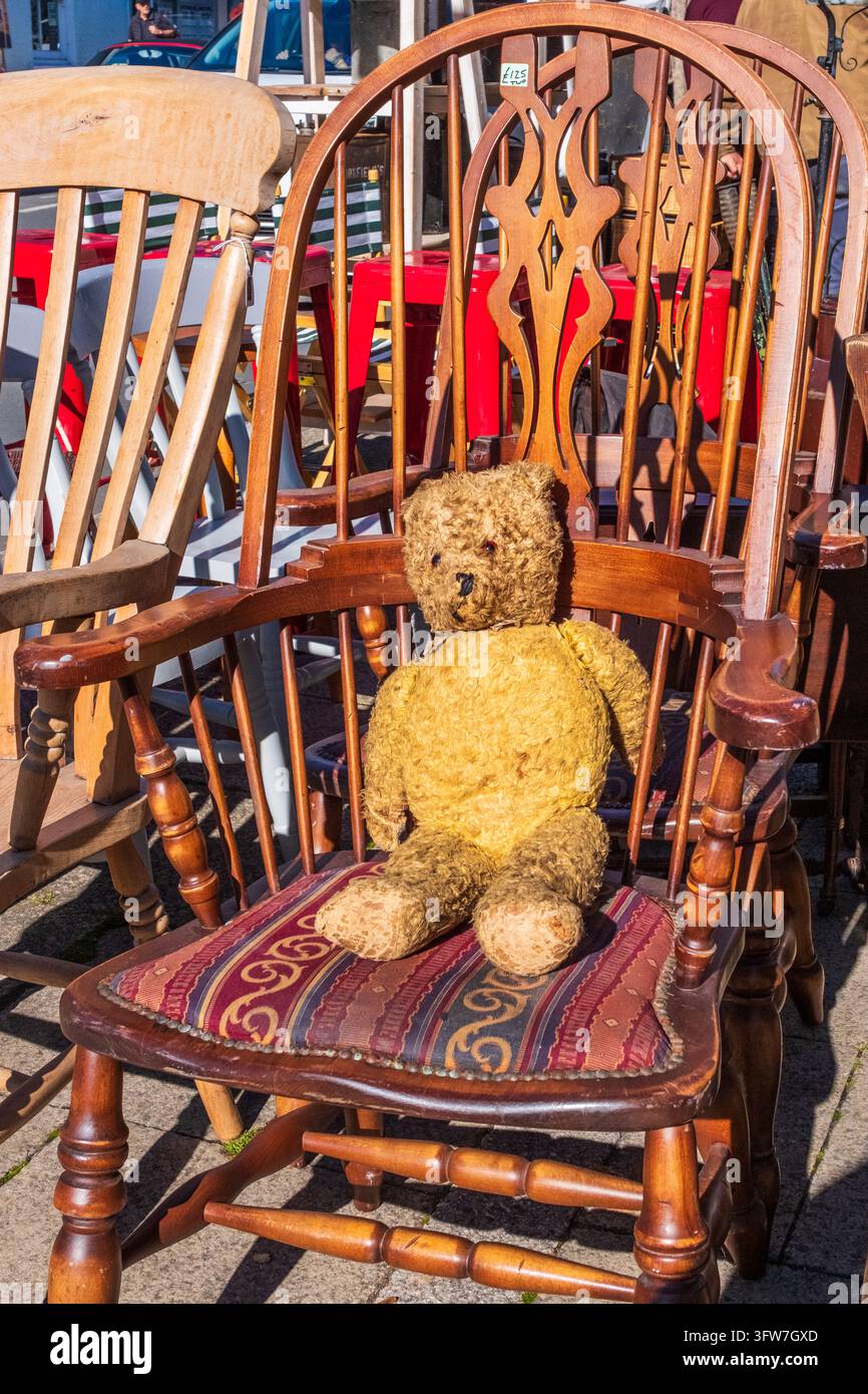 Orso di peluche antico, amato e consumato, appoggiato su una poltrona intagliata in legno vintage in un mercatino delle pulci all'aperto a Bridport, Dorset, Inghilterra. Foto Stock