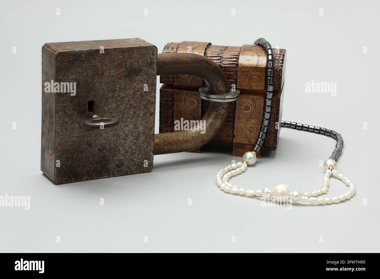 Grande serratura a padlock bloccata con una chiave e un baule del tesoro in miniatura intagliato. Gioielli di imitazione. Sfondo neutro. Foto Stock
