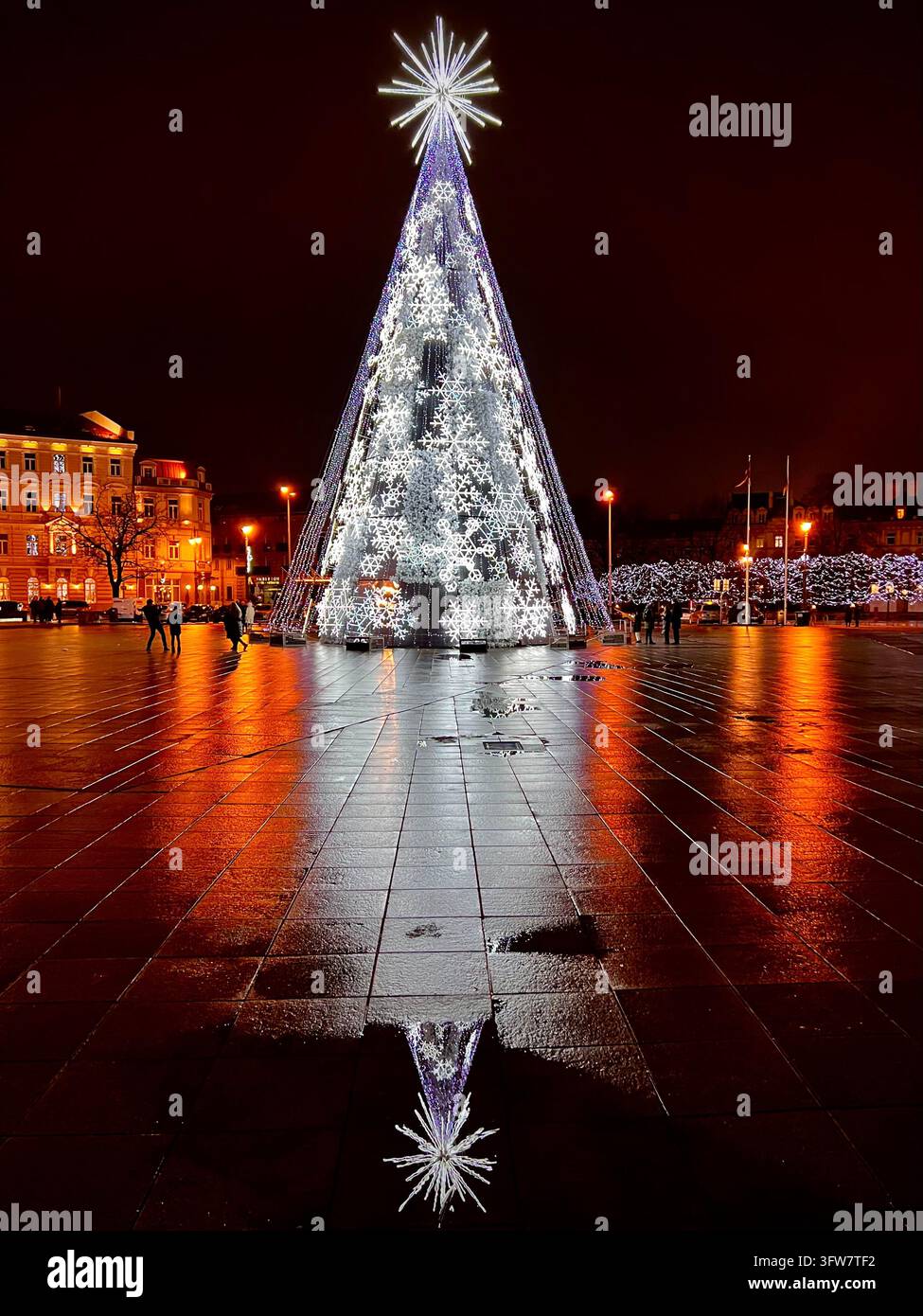 Albero di Natale su Piazza della Cattedrale a Vilnius, con intricate installazioni luminose a forma di fiocco di neve bianco, una stella apicale luminosa e riflessi brillanti - Immagine stock catturata con smartphone