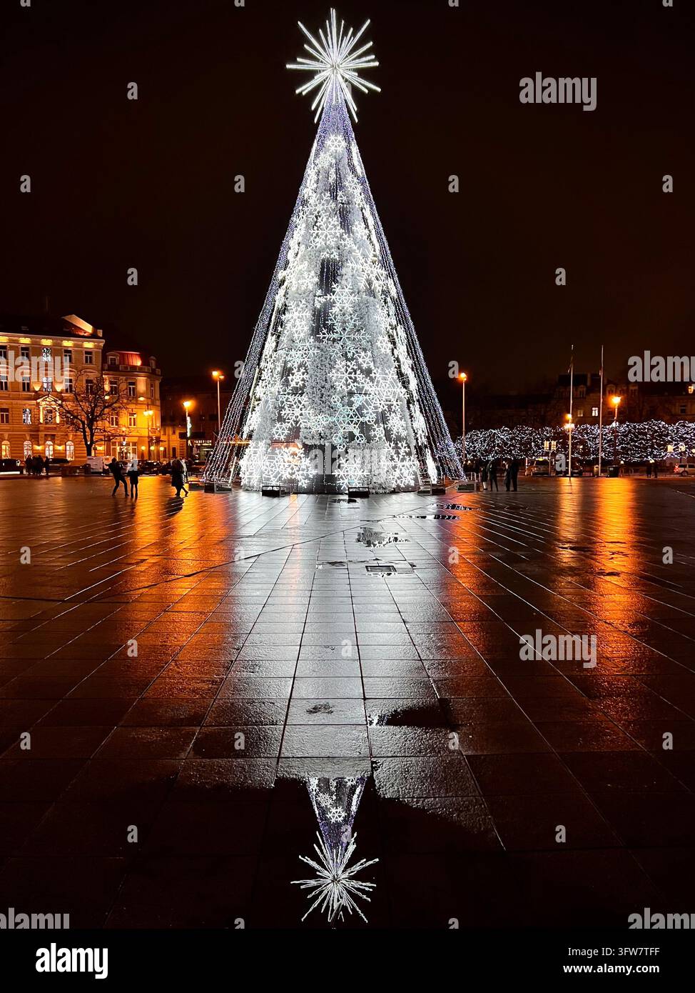 Albero di Natale su Piazza della Cattedrale a Vilnius, con intricate installazioni luminose a forma di fiocco di neve bianco, una stella apicale luminosa e riflessi brillanti - Immagine stock catturata con smartphone